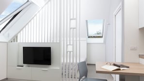 A modern, well-lit room with a TV mounted on a white cabinet, a desk with a chair, and a window providing a view of the outdoors. - CIRENE APARTMENTS (Milan)
