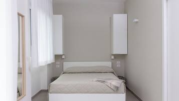 Un dormitori petit i modern amb llit, taules de nit i un mirall.