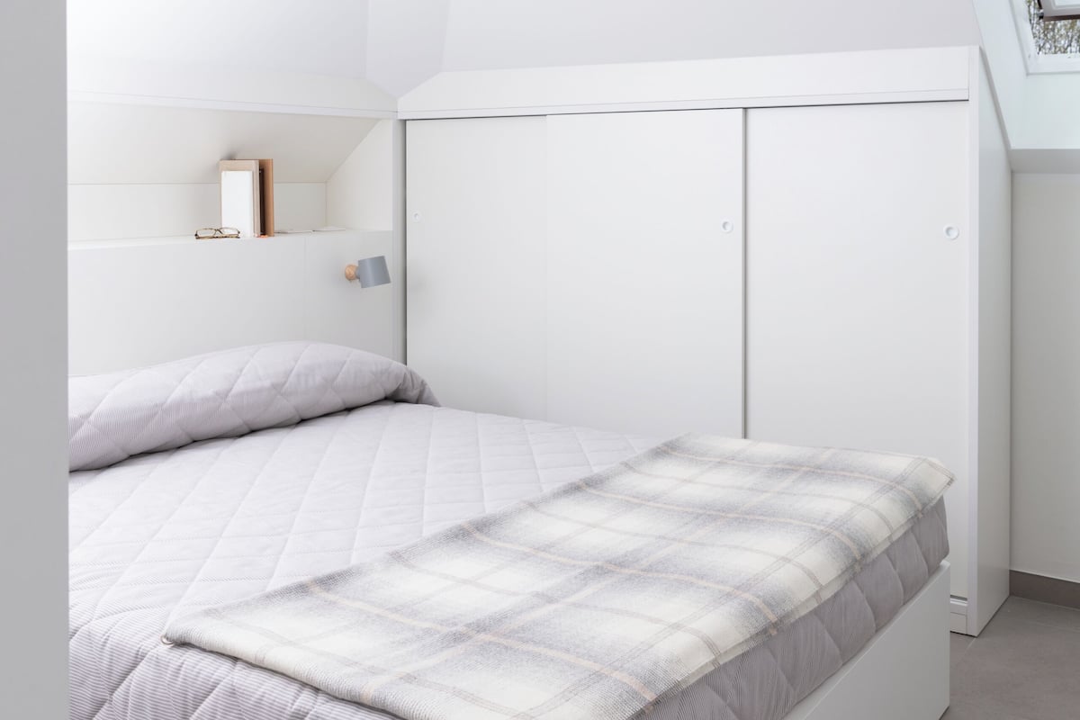 A modern bedroom with a white bed, a slanted ceiling, and a skylight.