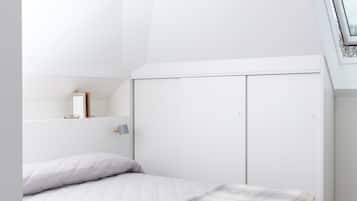 A modern bedroom with a white bed, a slanted ceiling, and a skylight.