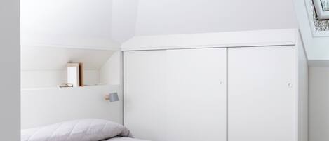 A modern bedroom with a white bed, a slanted ceiling, and a skylight.