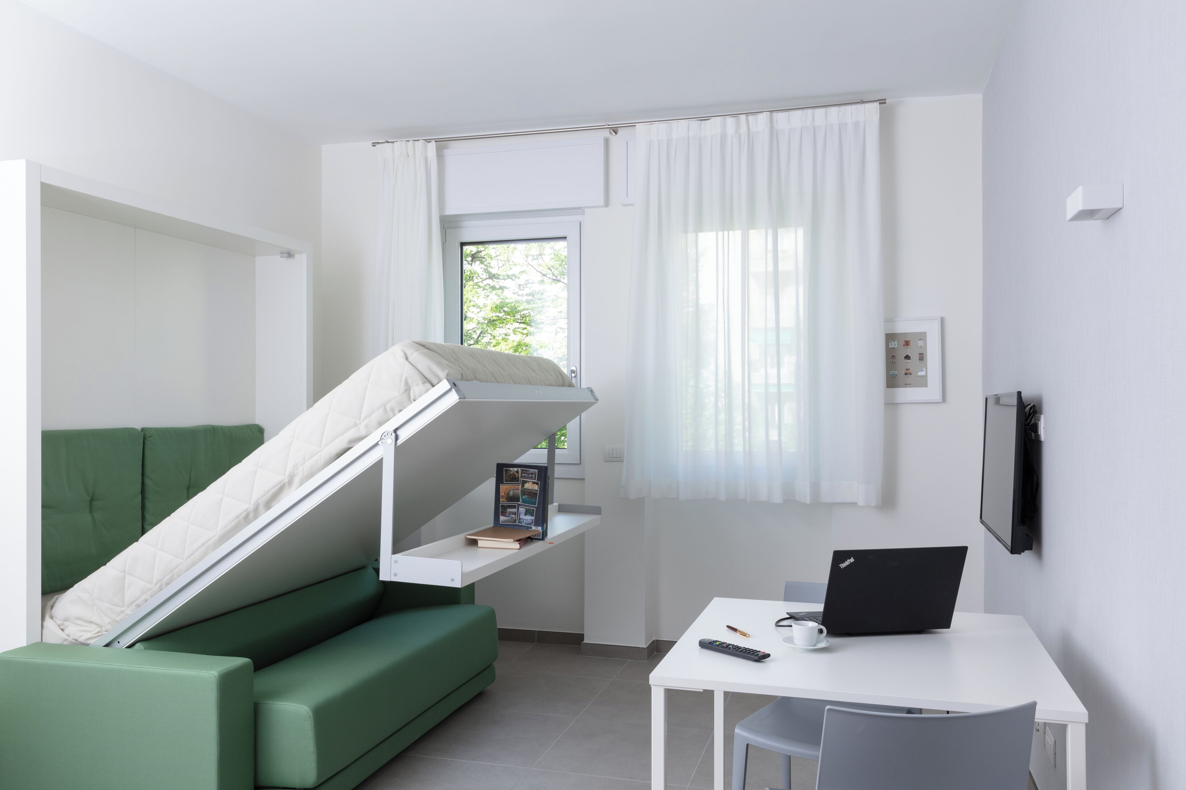 Ein kleiner Raum mit einem grünen Sofa, einem Tisch mit einem Laptop und einem Fenster mit Vorhängen.