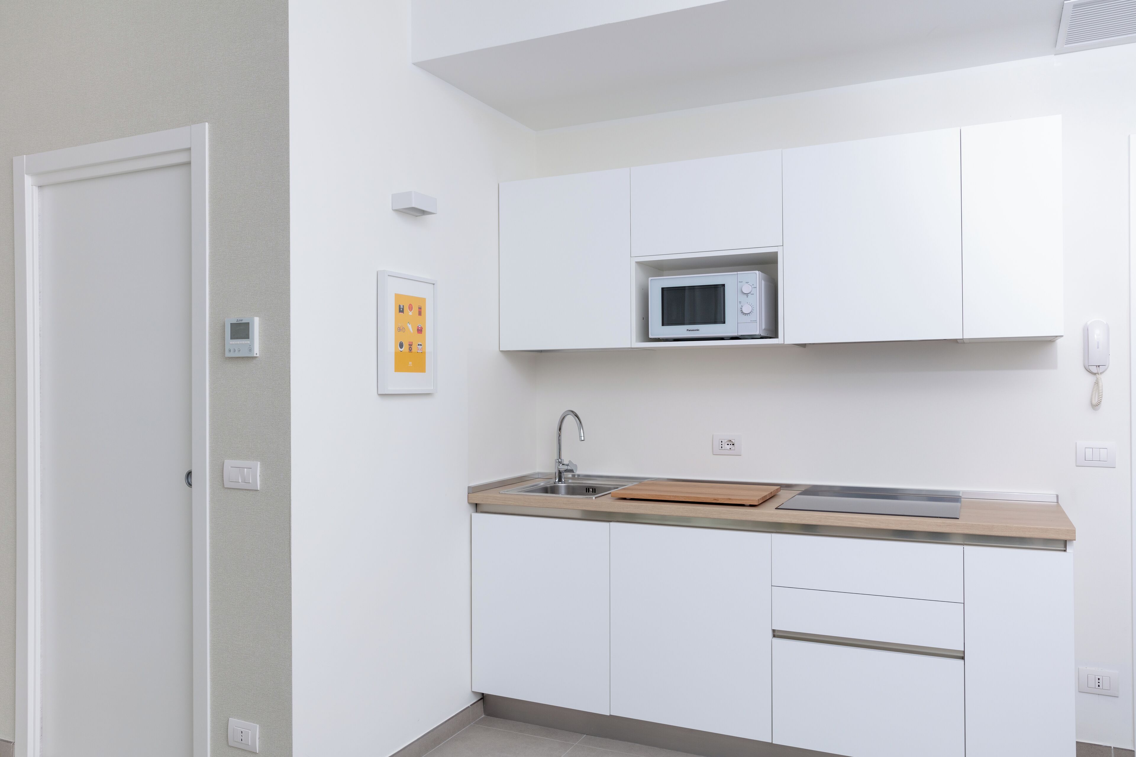A modern kitchen with white cabinets, a microwave, a sink, and a wooden countertop.