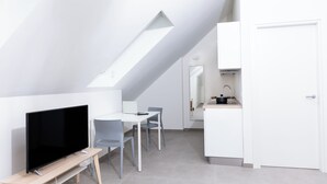 A modern, minimalist room with a sloped ceiling, a flat-screen TV on a wooden stand, a dining table with chairs, and a kitchen area with a sink and cabinets. - CIRENE APARTMENTS (Milan)