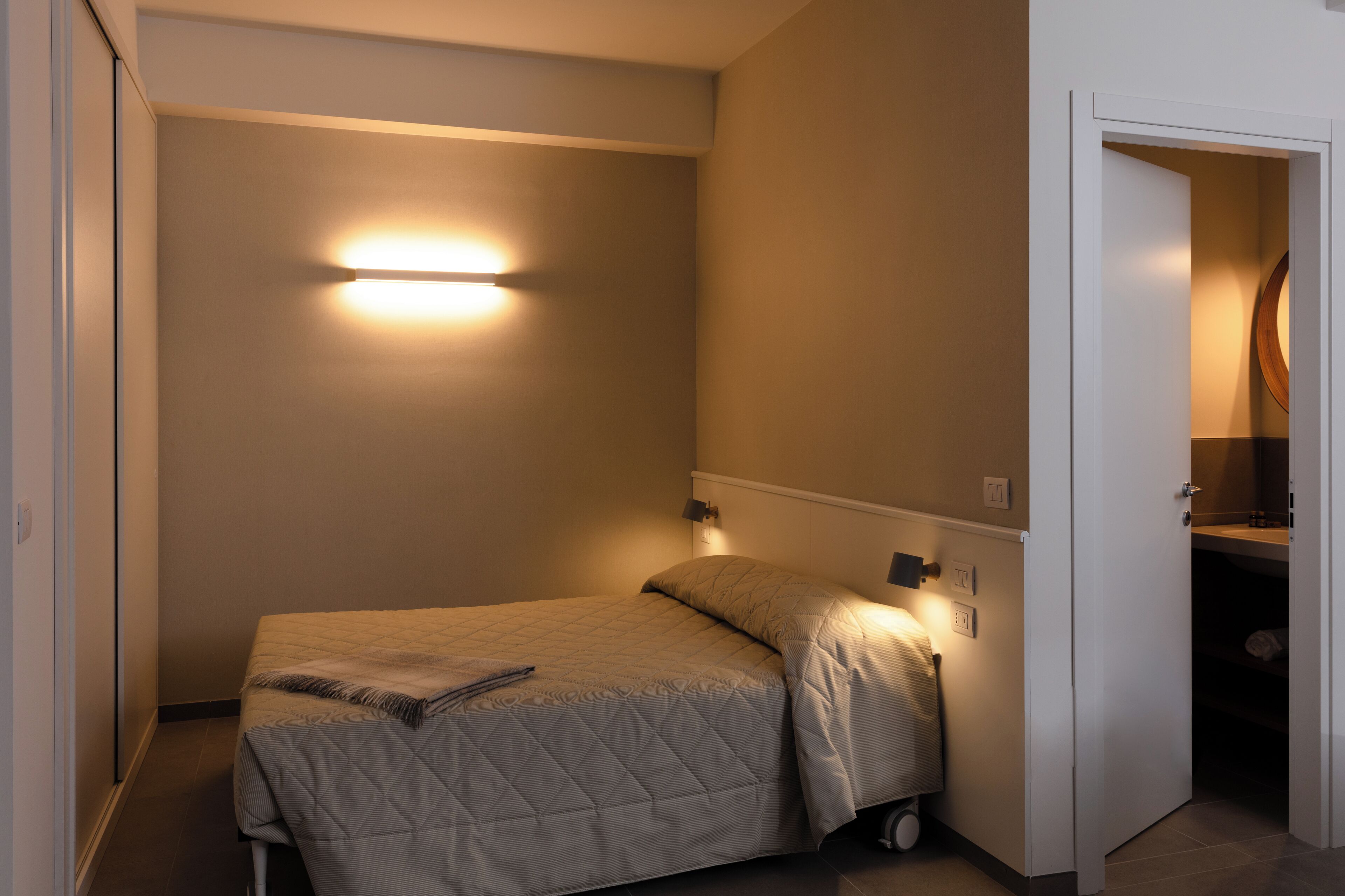 Un dormitorio pequeño y ordenado con cama, lámparas de noche y un armario visible.