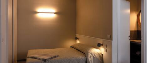 Un dormitorio pequeño y ordenado con cama, lámparas de noche y un armario visible.