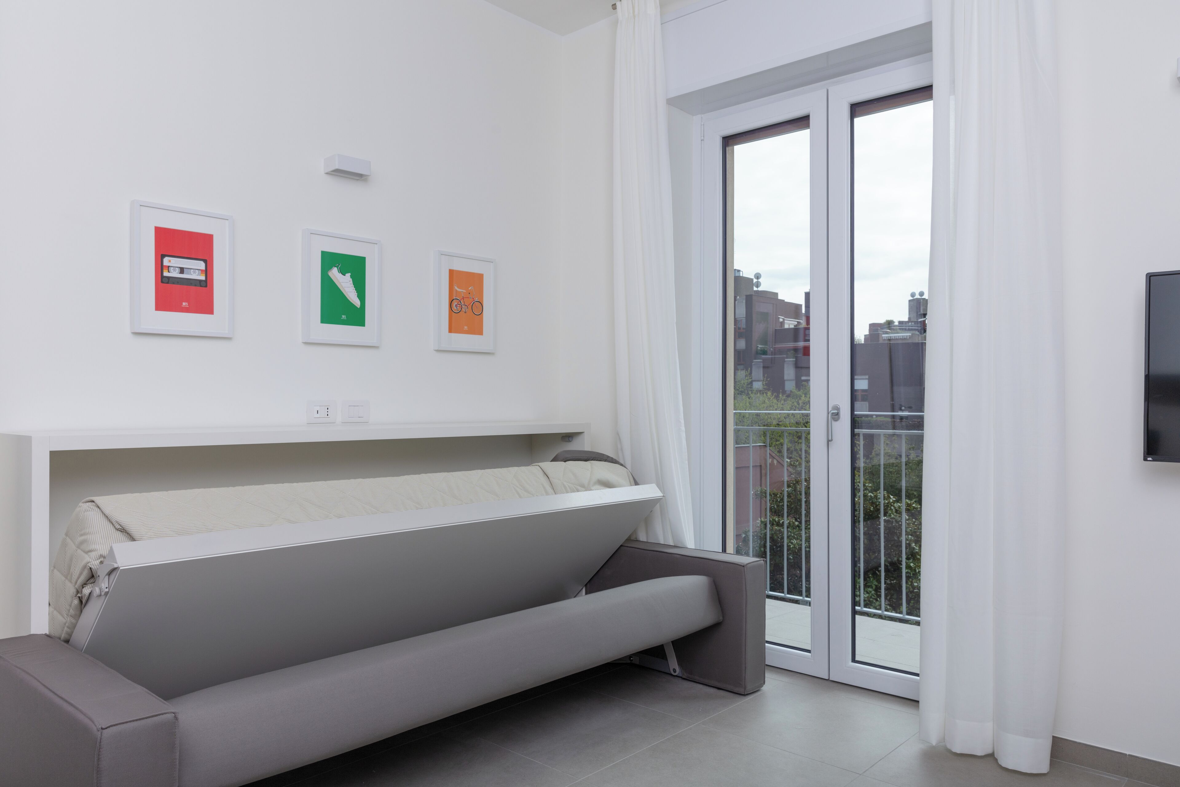 Una sala de estar moderna con un sofá, un televisor de pantalla plana y un ventanal corredizo a un balcón.