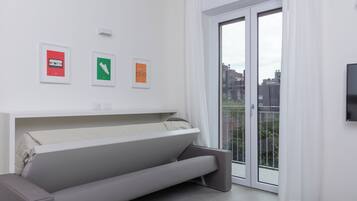 Una sala de estar moderna con un sofá, un televisor de pantalla plana y un ventanal corredizo a un balcón.