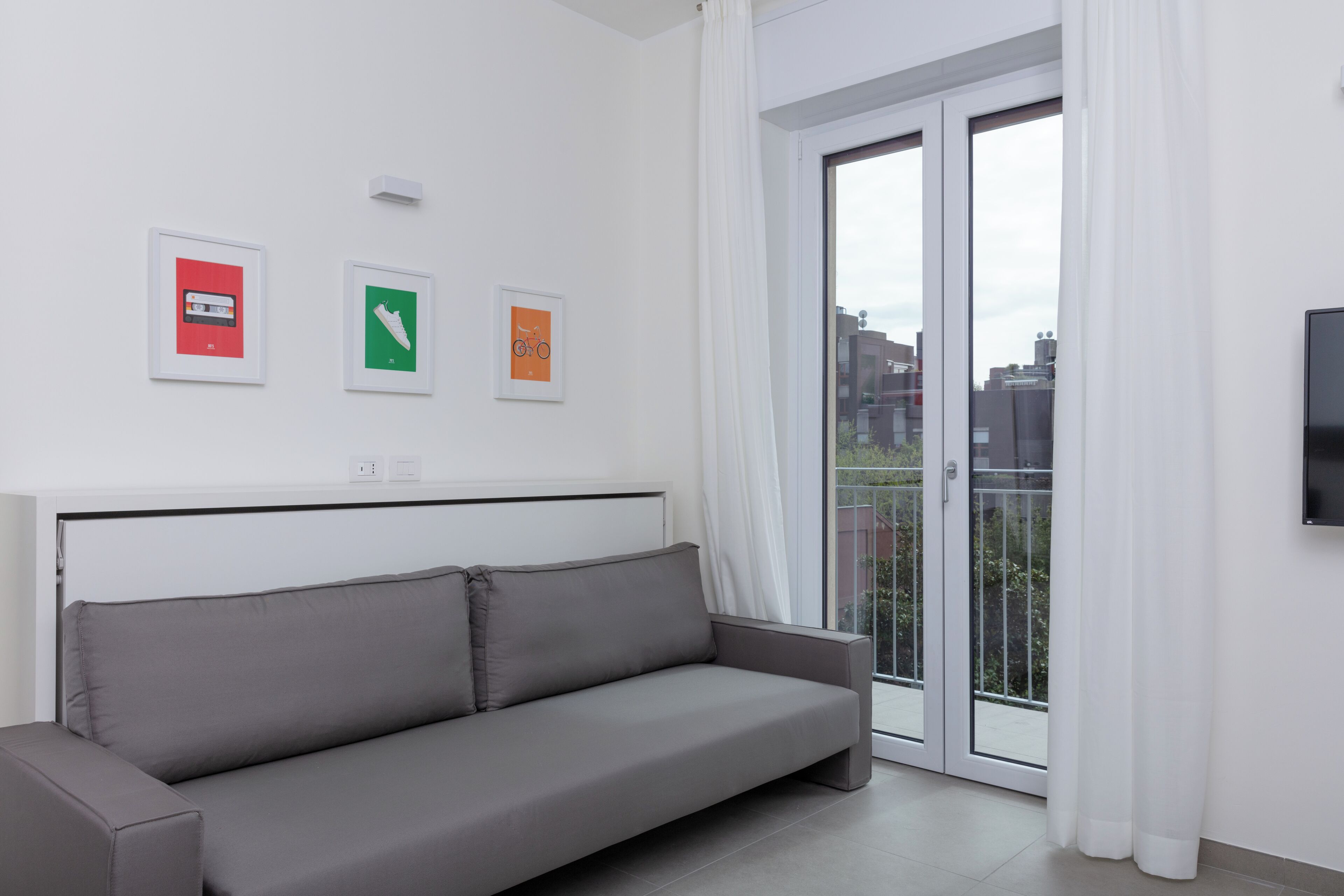 A modern living room with a grey sofa, a flat-screen TV, and a sliding glass door to a balcony.