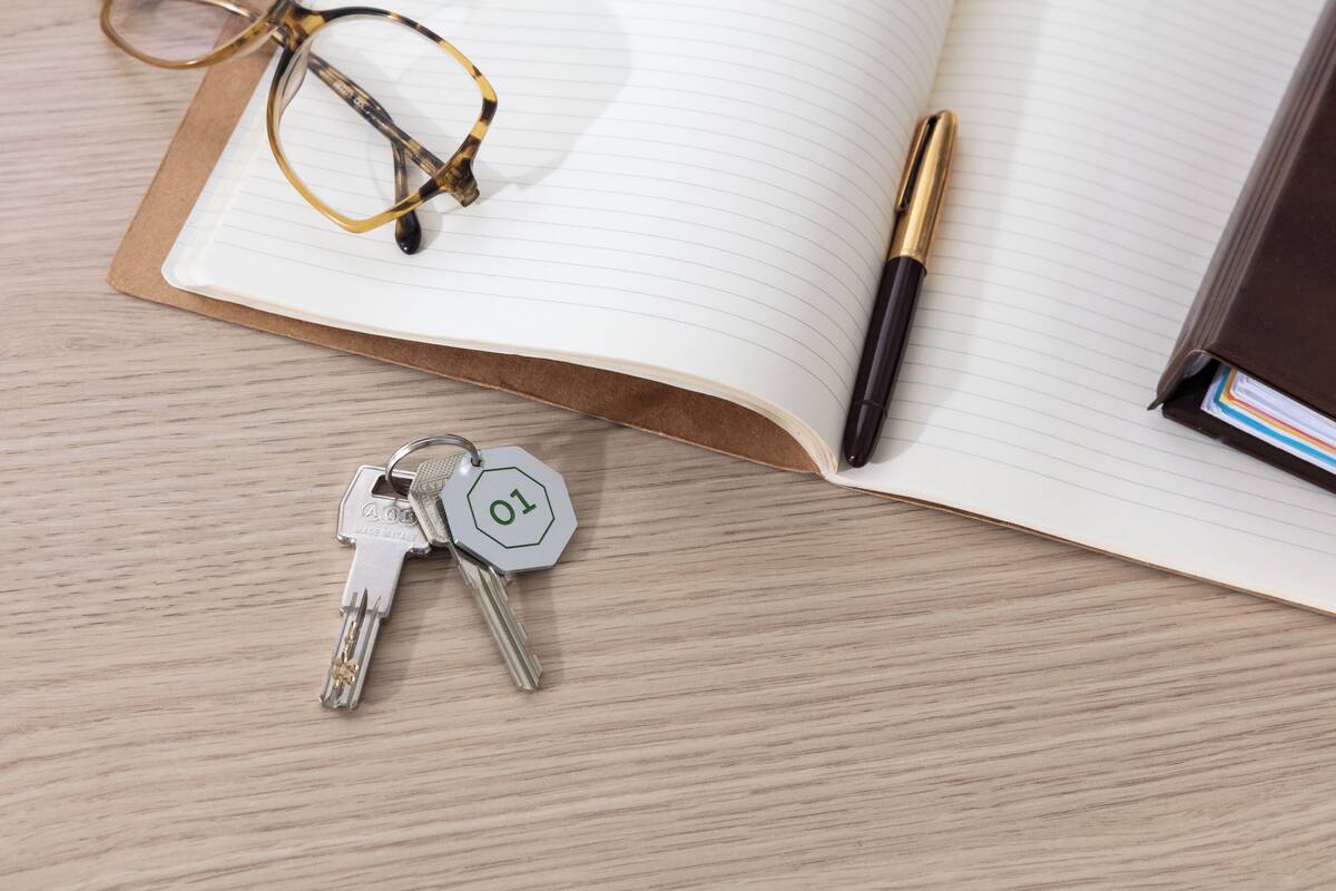 A notebook with a pen, glasses, and keys on a wooden surface.