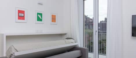 A modern room with a sofa bed, a flat-screen TV, and a sliding glass door to the outside.