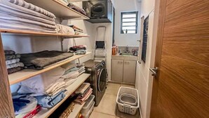 Een wasserette met planken vol opgevouwen kleding, een wasmachine, een droger en een klein raam.