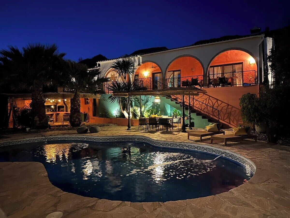 A pool area with a staircase leading to a building with arched windows and outdoor seating.
