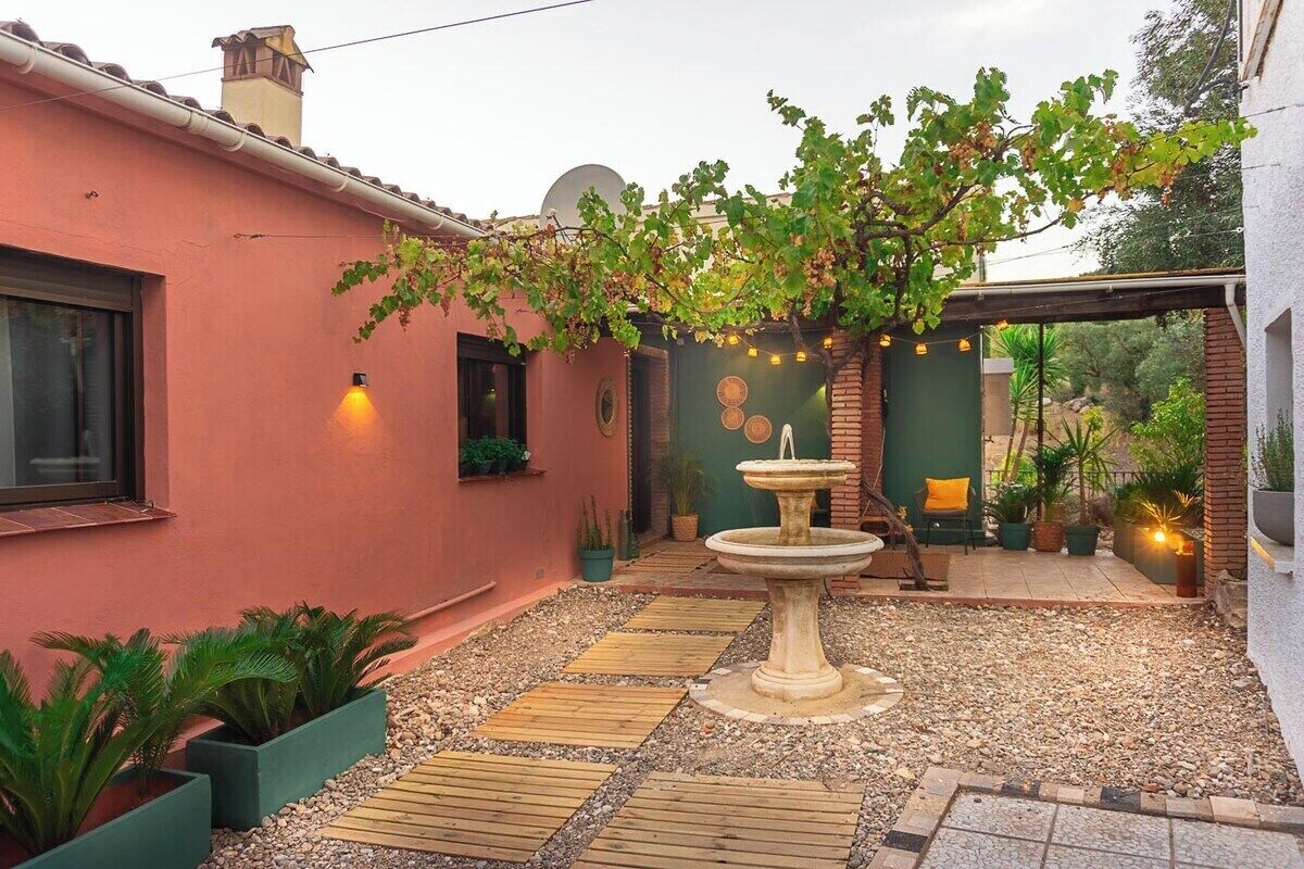 A courtyard with a stone fountain, wooden walkways, and potted plants.