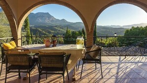Una terraza con mesa y sillas, vista a las montañas y una estructura de pérgola.