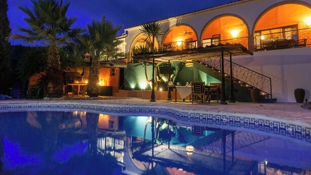 Un hotel con piscina, asientos exteriores y terraza cubierta.