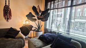 A living room with a sofa, a coffee table, a potted plant, and a window with a view of buildings. - Enjoyable 3-bedroom apartment with terrace in the center of Ghent (Gent)