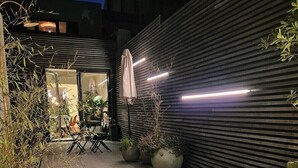 An outdoor patio area with a modern design, featuring a metal wall, potted plants, and a seating area with a round table and chairs. - Enjoyable 3-bedroom apartment with terrace in the center of Ghent (Gent)