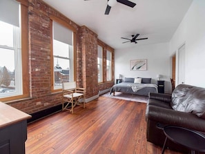 Une pièce avec un mur en briques, un plancher en bois, un lit, un canapé en cuir, un bureau et une chaise.