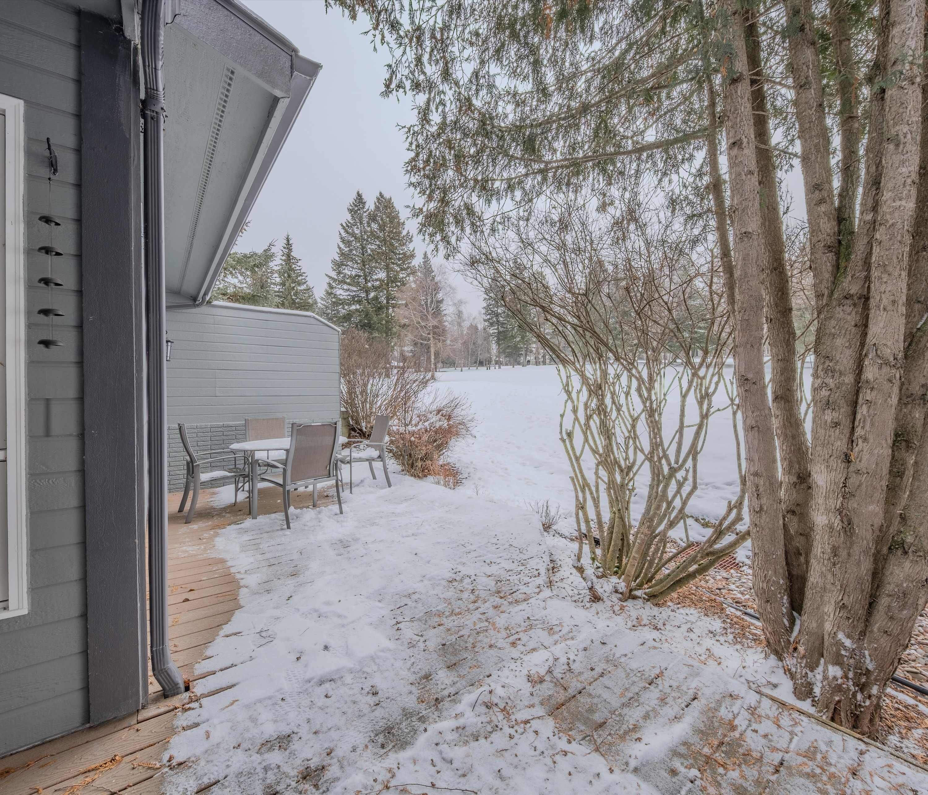 A covered patio with a table and chairs, a wooden deck, and a snow-covered yard with trees.