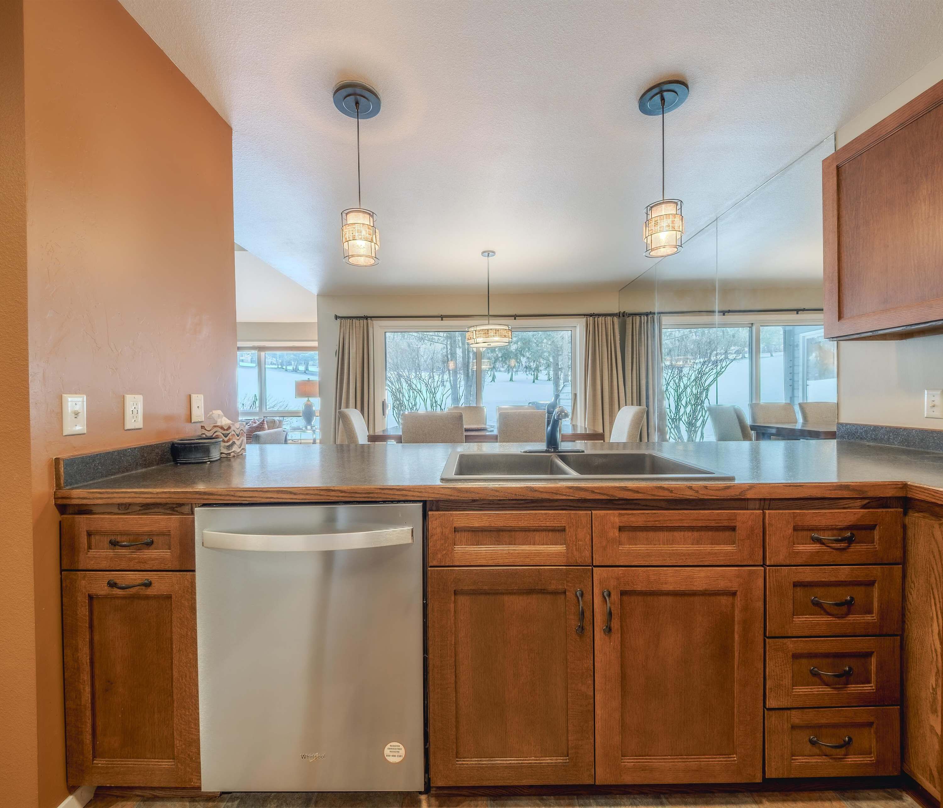A modern kitchen with wooden cabinets, a stainless steel dishwasher, and pendant lighting.