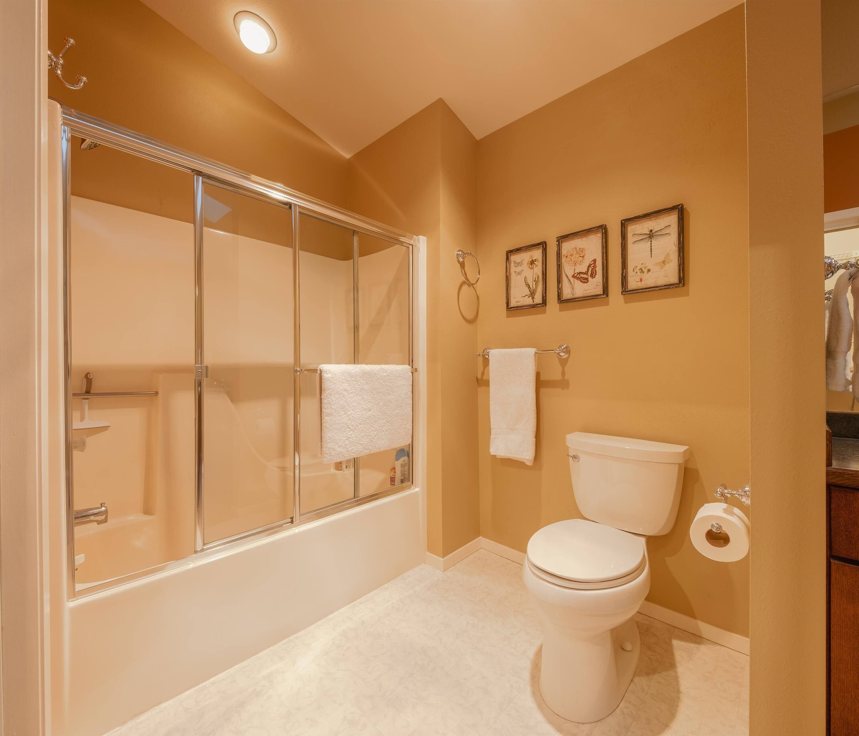 A bathroom with a glass-enclosed shower, a toilet, and three framed pictures on the wall.