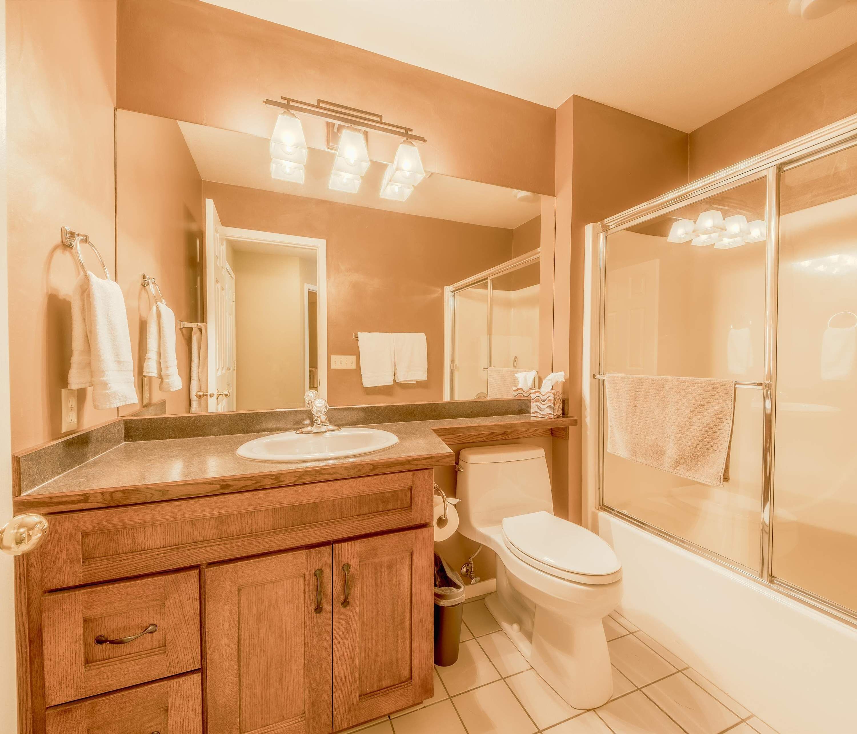 A bathroom with a wooden vanity, a sink, a toilet, and a glass shower enclosure.