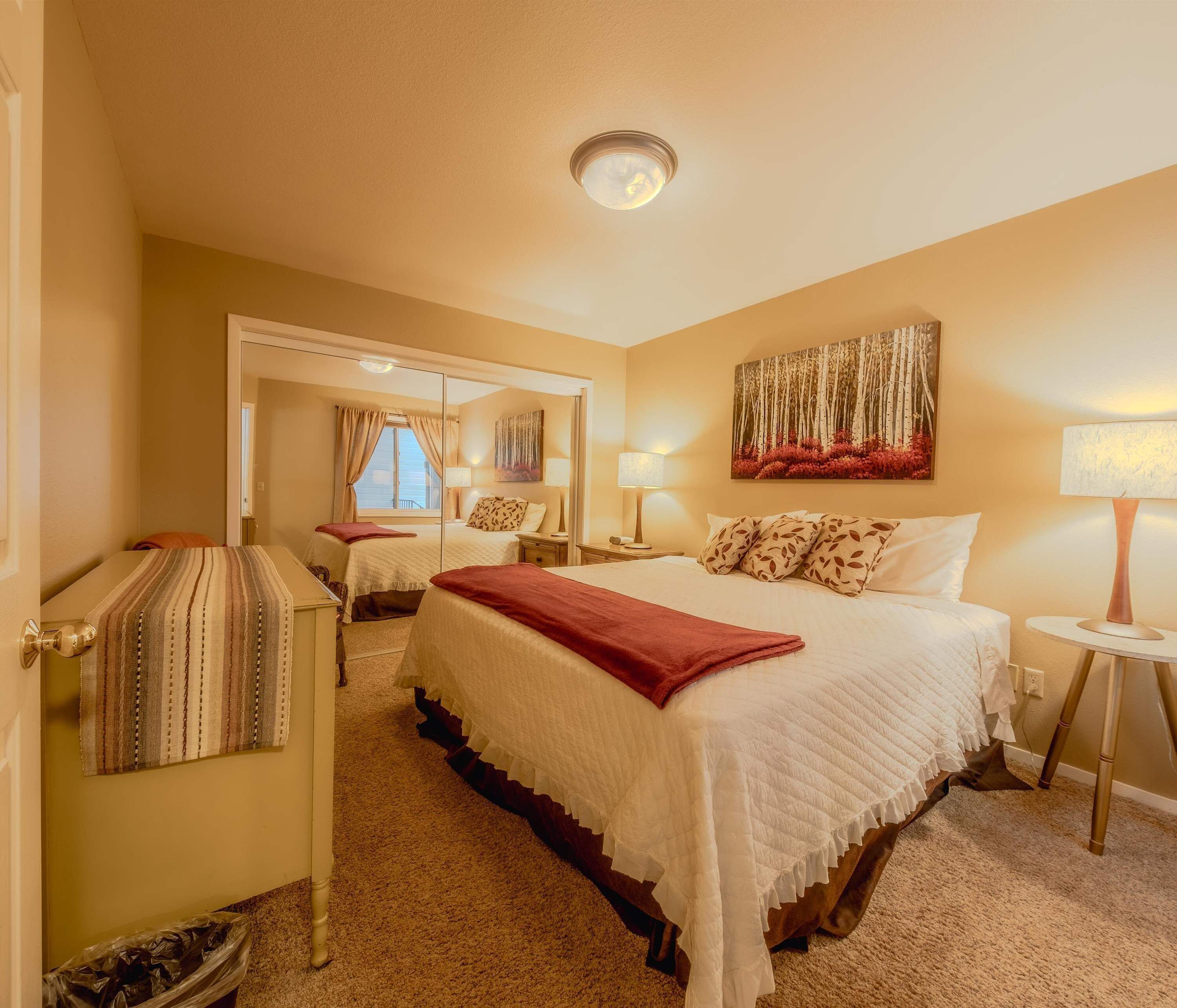 A hotel room with a large bed, a bedside table with a lamp, a mirror, and a painting on the wall.