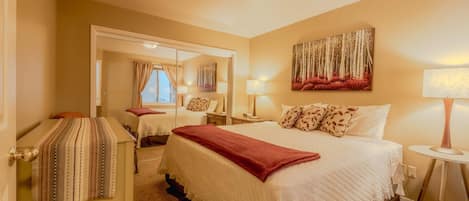 A hotel room with a large bed, a bedside table with a lamp, a mirror, and a painting on the wall.