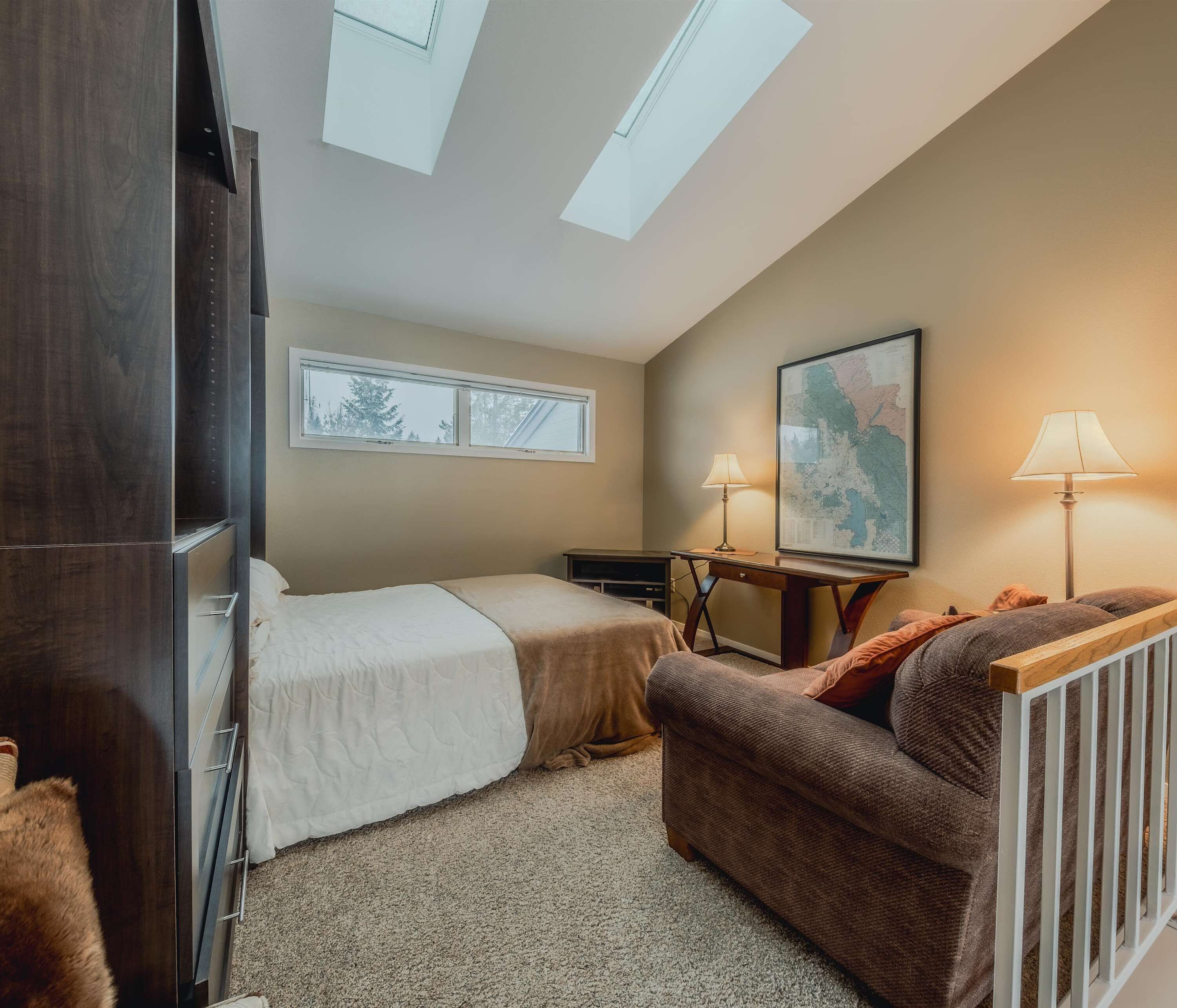 A bedroom with two beds, a desk, a chair, a map on the wall, and skylights.