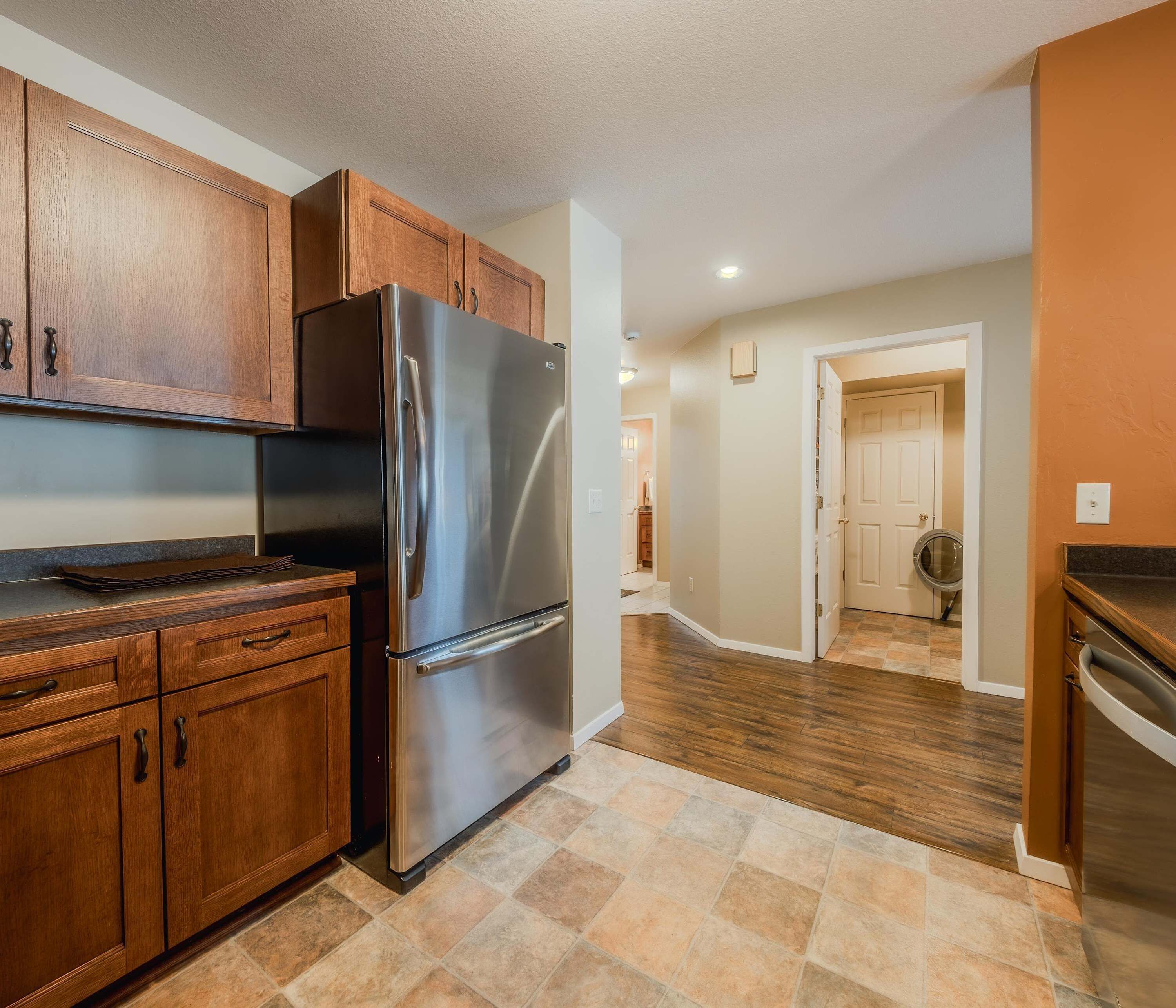 A kitchen with wooden cabinets, a stainless steel refrigerator, and a tiled floor.