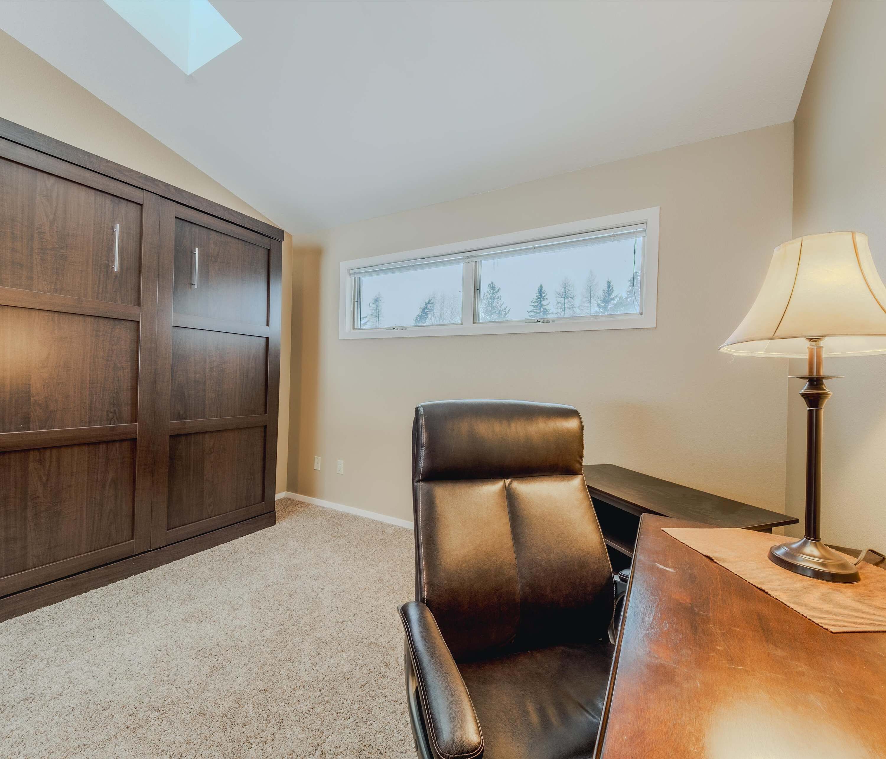A room with a dark brown leather chair, a wooden desk, a lamp, and a wardrobe.