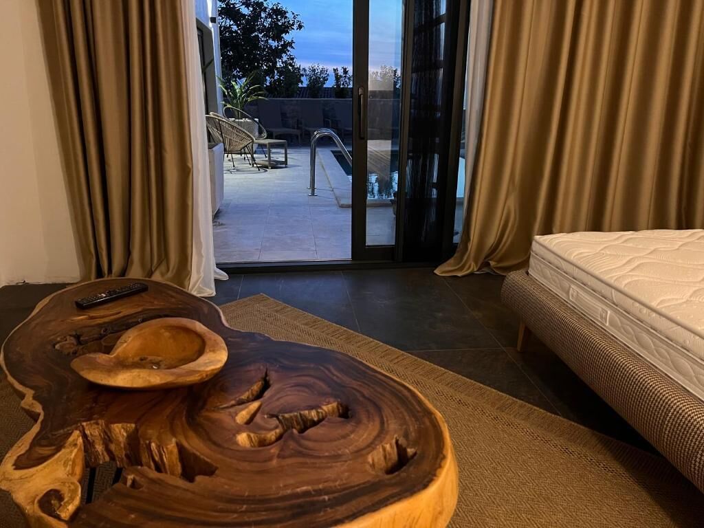 Ein Zimmer mit einem großen Holztisch, einem Bett und Blick auf eine Terrasse mit Stühlen und einem Pool.