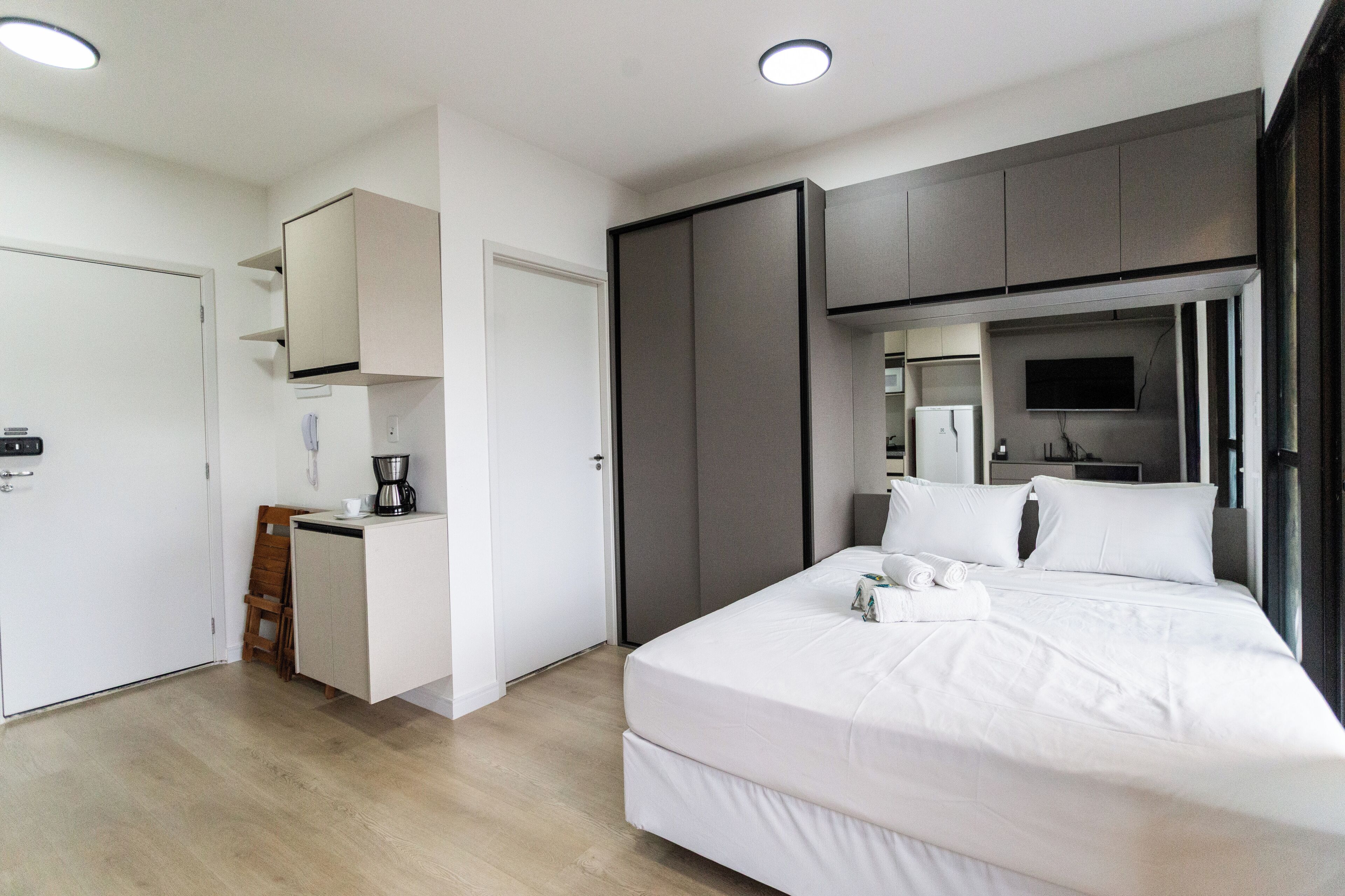 A modern hotel room with a bed, a desk, a chair, a wardrobe, and a television.