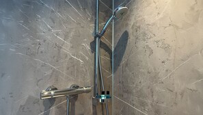 Une douche équipée d’un pommeau de douche à main, d’un robinet mural et d’un distributeur de savon.