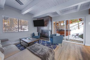 Ein modernes Wohnzimmer mit Kamin, blauen Sofas und einem großen Fenster mit Jalousien.