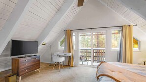 A bedroom with a sloped ceiling, a bed, a desk, a TV, and a balcony with curtains. - Zephyr Chalet Steps from Zephyr Cove (Glenbrook)