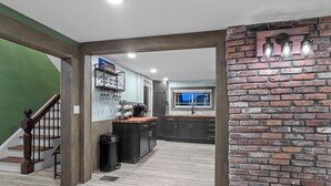A modern kitchen with dark cabinets, a wooden staircase, and a brick accent wall.