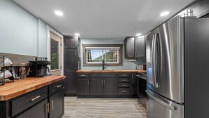 A modern kitchen with dark cabinetry, a stainless steel refrigerator, and a wooden countertop.