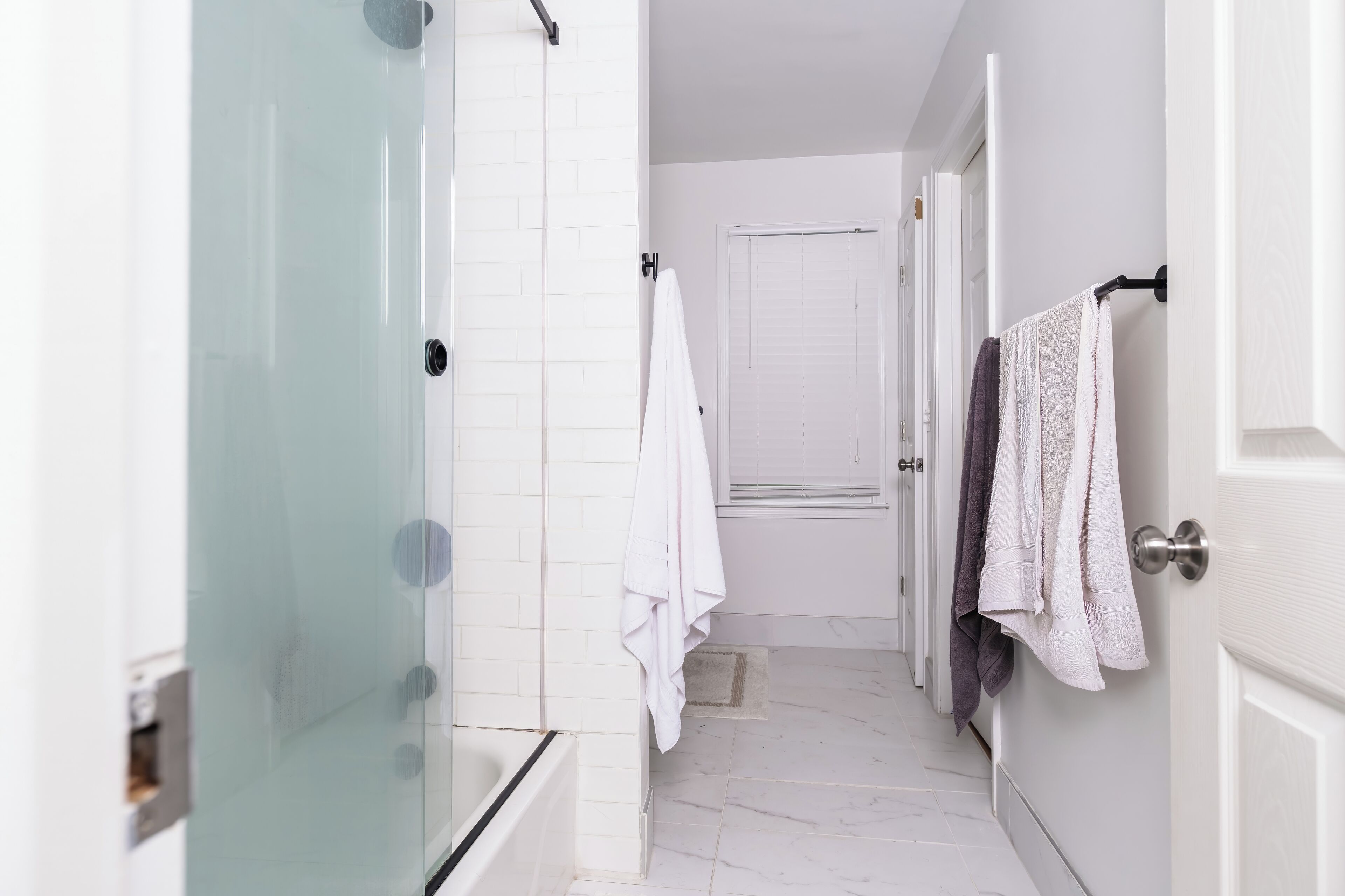 A modern bathroom with a glass shower enclosure, white tiled walls, and a white door.