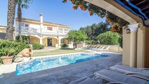 Una piscina con sillas de descanso, un edificio con balcón y un jardín con palmeras.