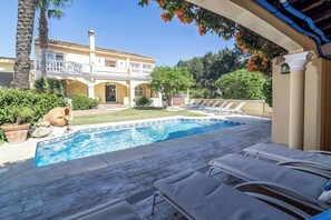 Ein Pool mit Liegestühlen, ein Gebäude mit Balkon und ein Garten mit Palmen.