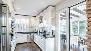 Una cocina moderna con armarios blancos, una isla central y un comedor visible a través de puertas de vidrio.