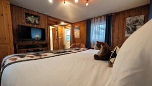 Ein Zimmer mit Holzwandverkleidung, einem Bett, einem Fernseher und einem Stofftier.