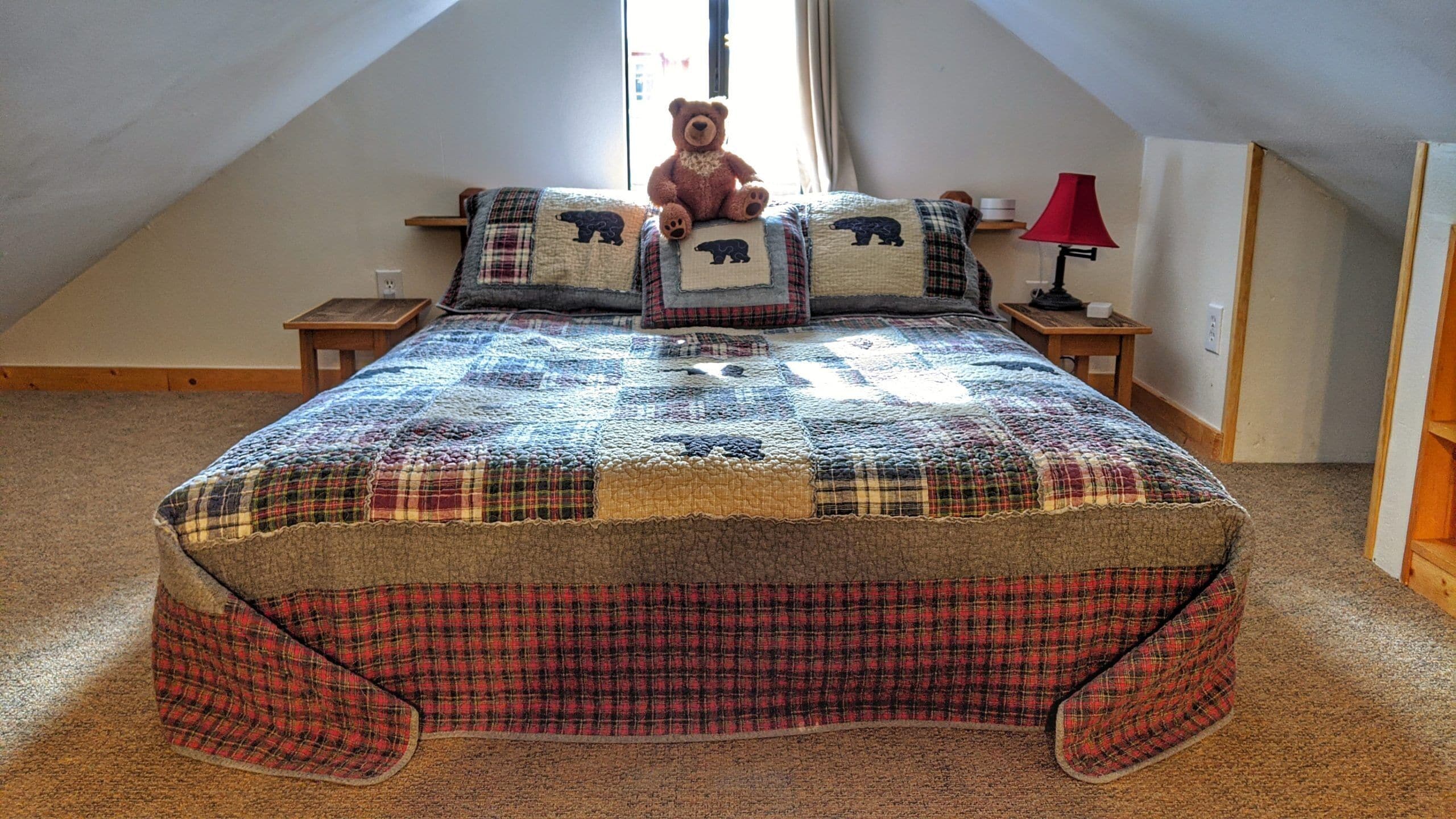 Ein Schlafzimmer mit einer gesteppten Bettdecke, einem Teddy auf dem Bett und einer Lampe auf dem Nachttisch.