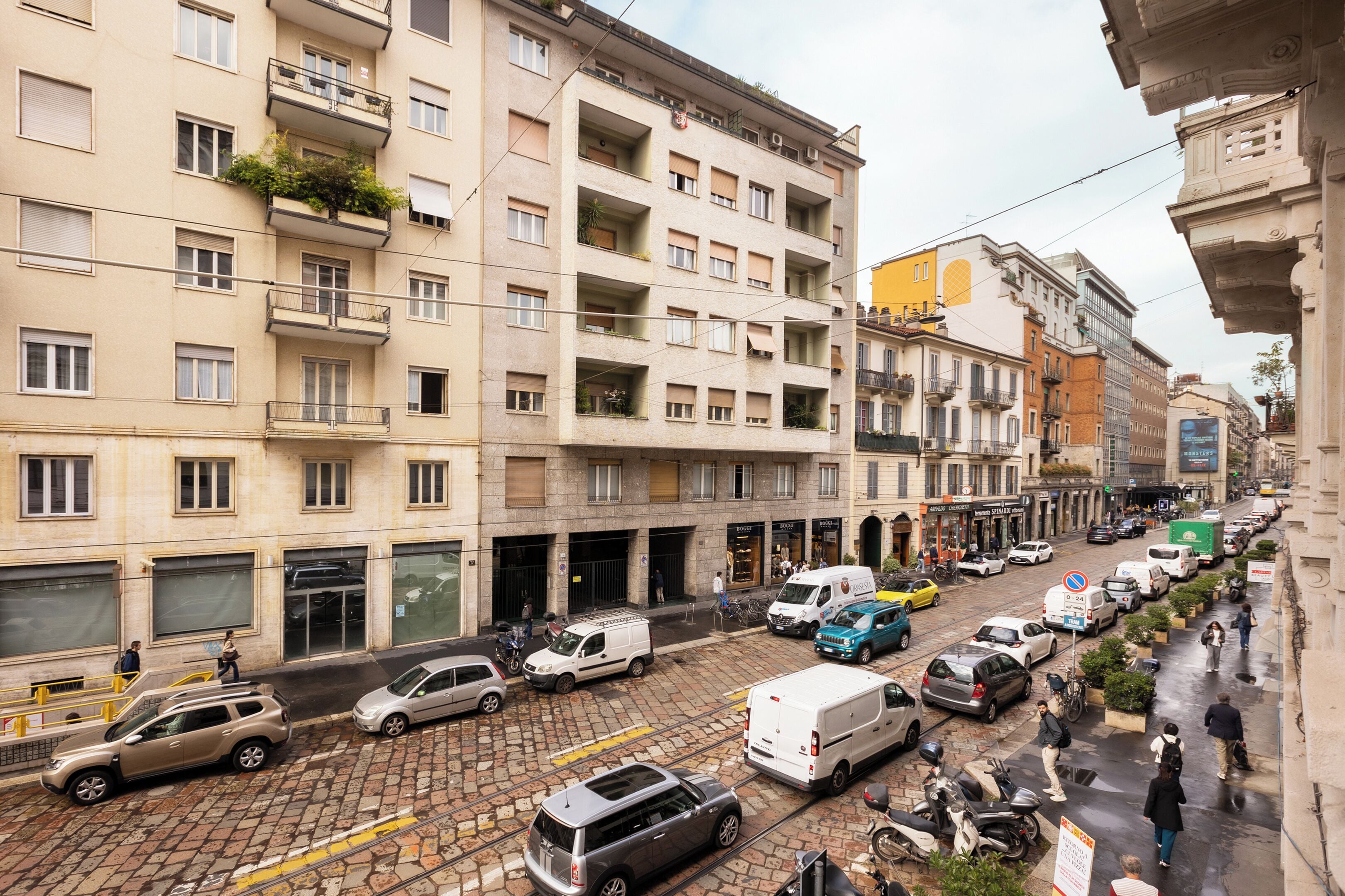 A multi-story building with balconies, a street with parked cars and a tram line.