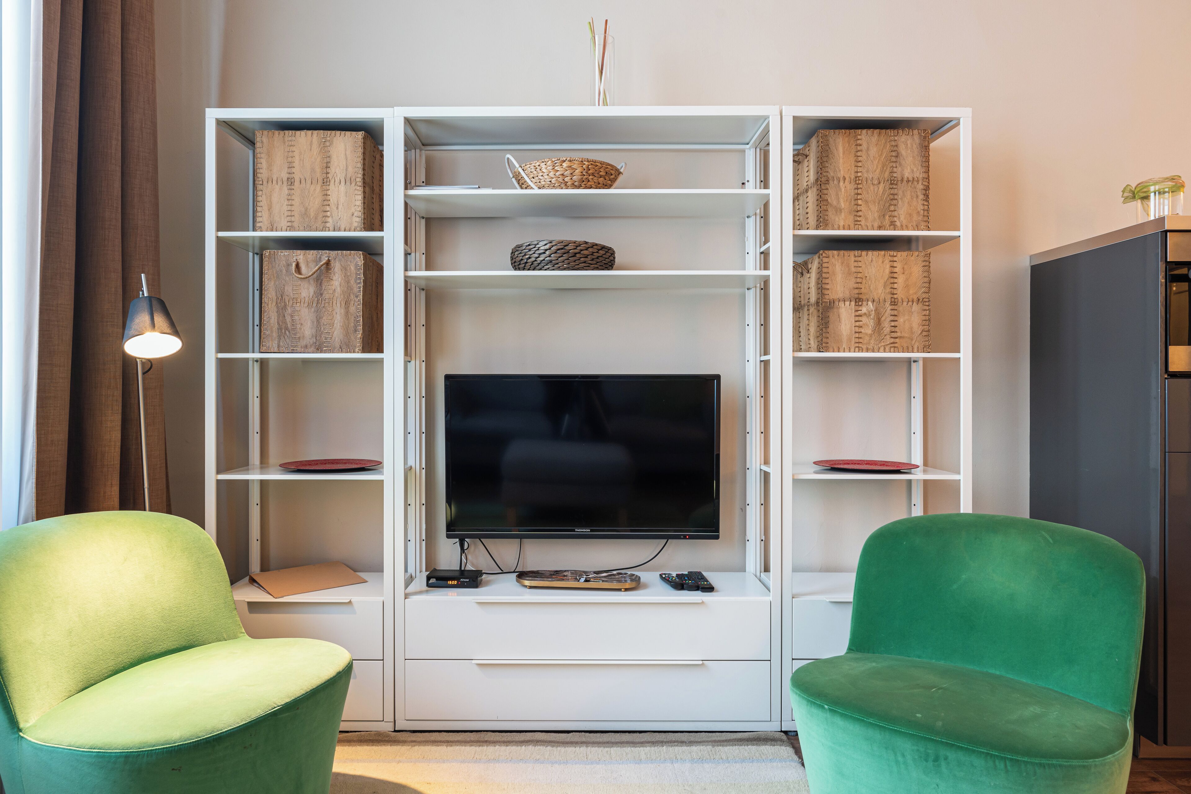 A living room with a TV, two green chairs, a white entertainment unit, and a lamp.