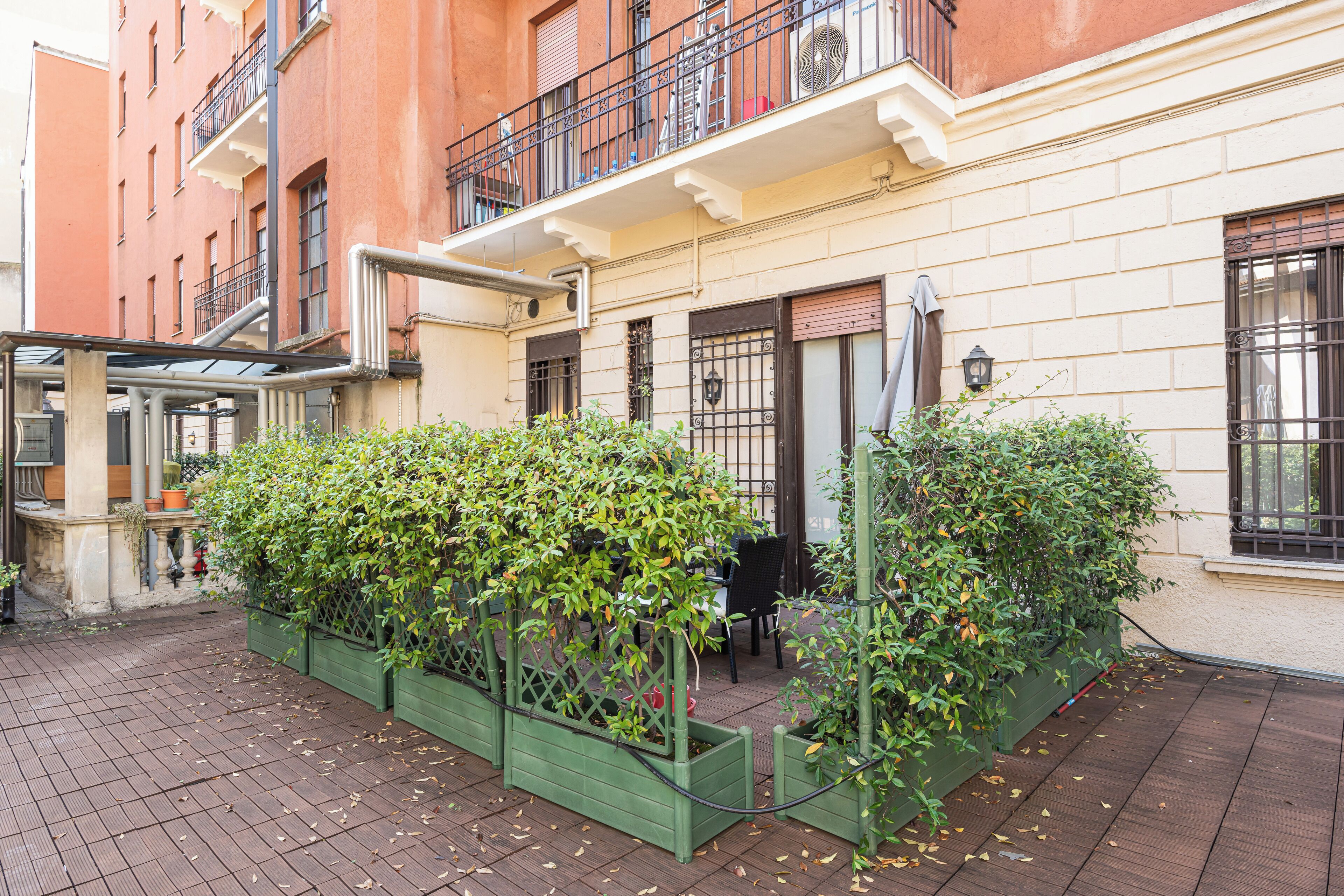 Un patio con un jardín verde, una zona de estar con sillas y un edificio con balcón.