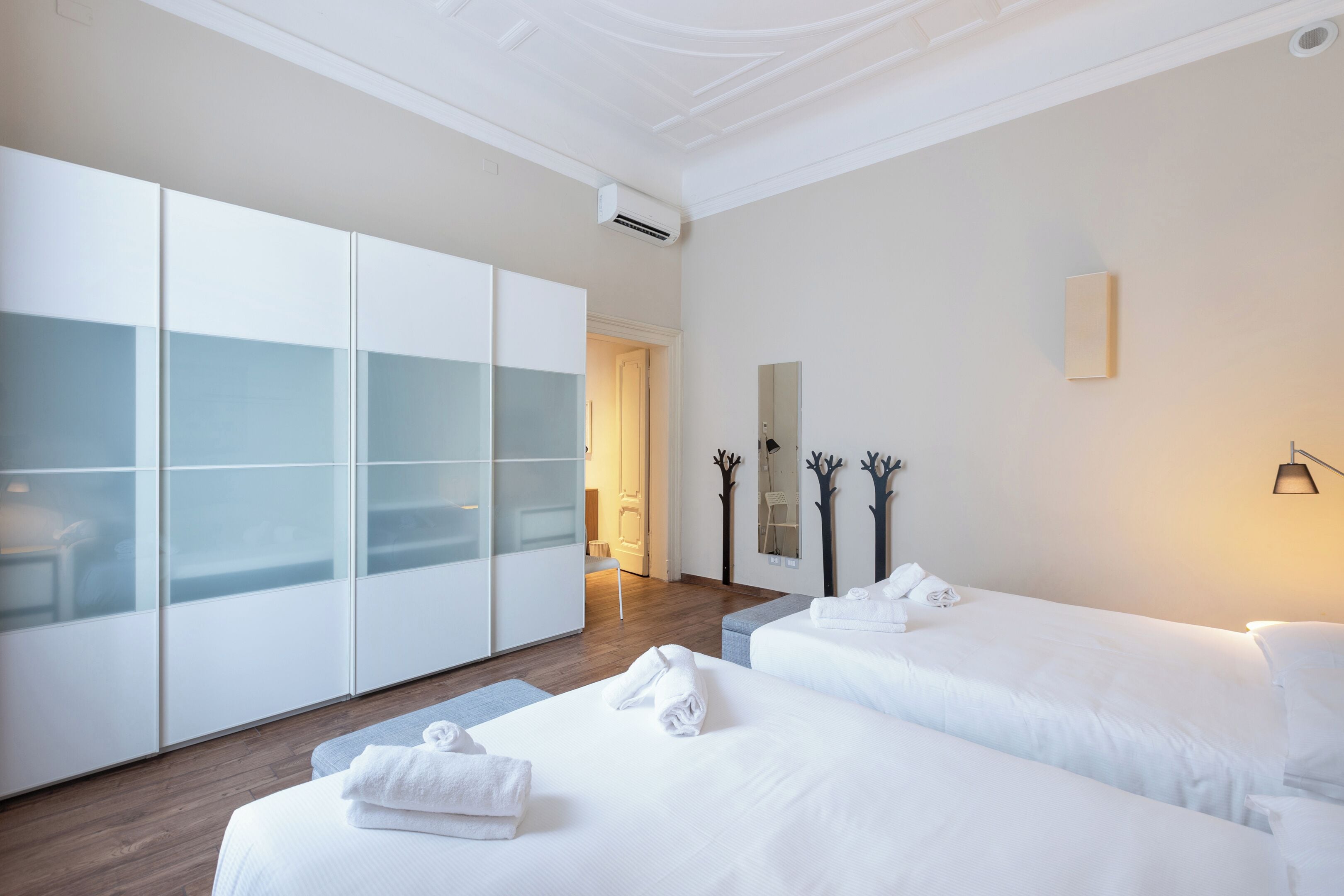 Habitación de hotel con dos camas, un armario, un espejo y una lámpara de pared.