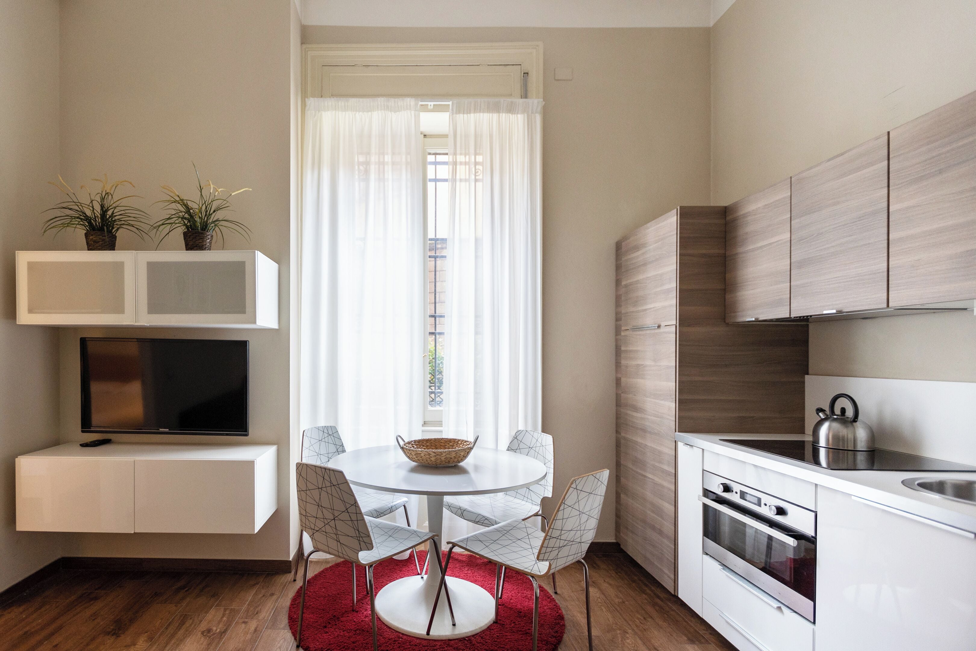 A modern kitchen with white cabinets, a built-in oven, and a kettle on the countertop.